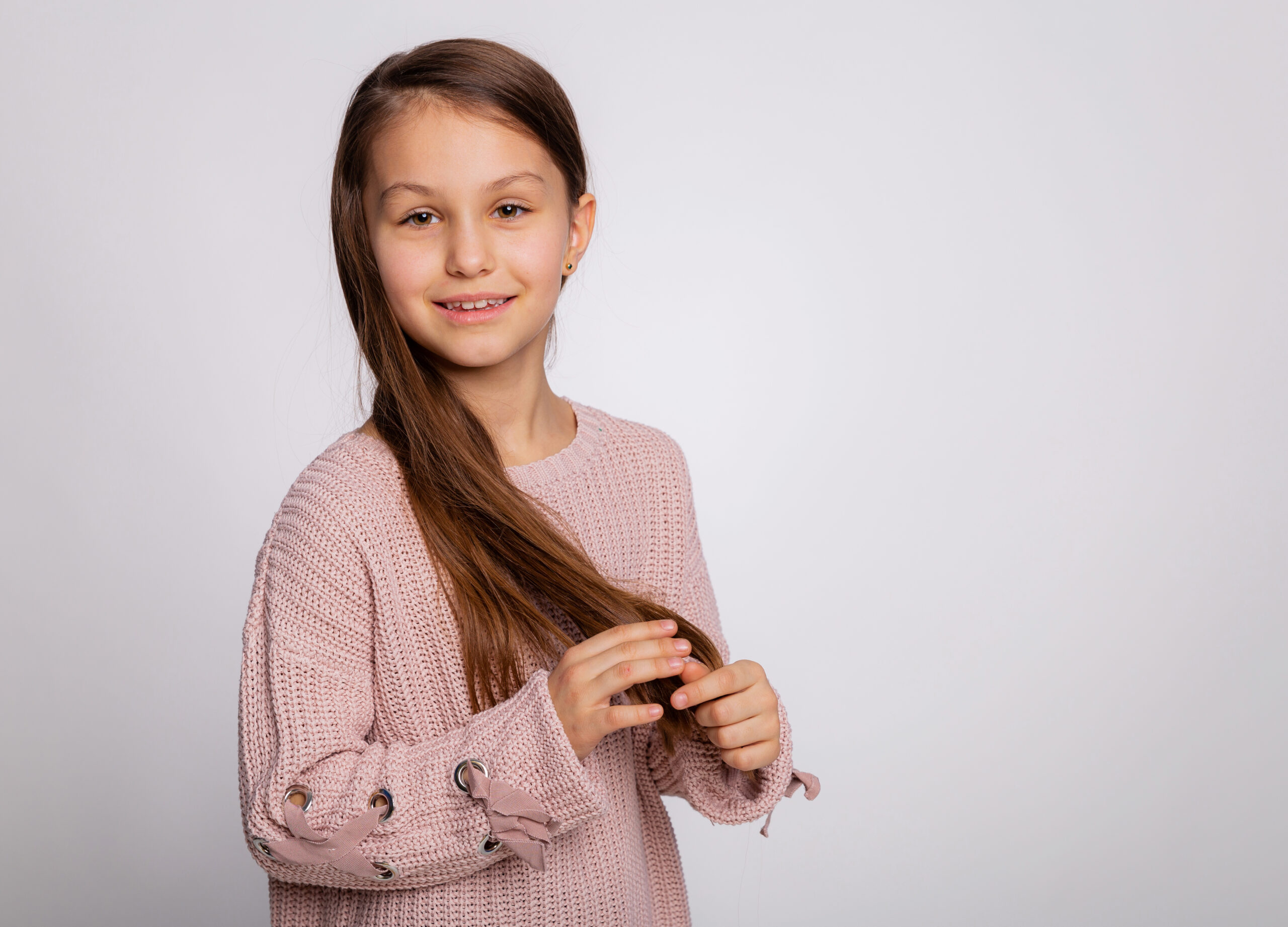 Portrait of a happy smiling child girl. Cute 8 years old girl face expression wearing pink sweater isolated over gray background